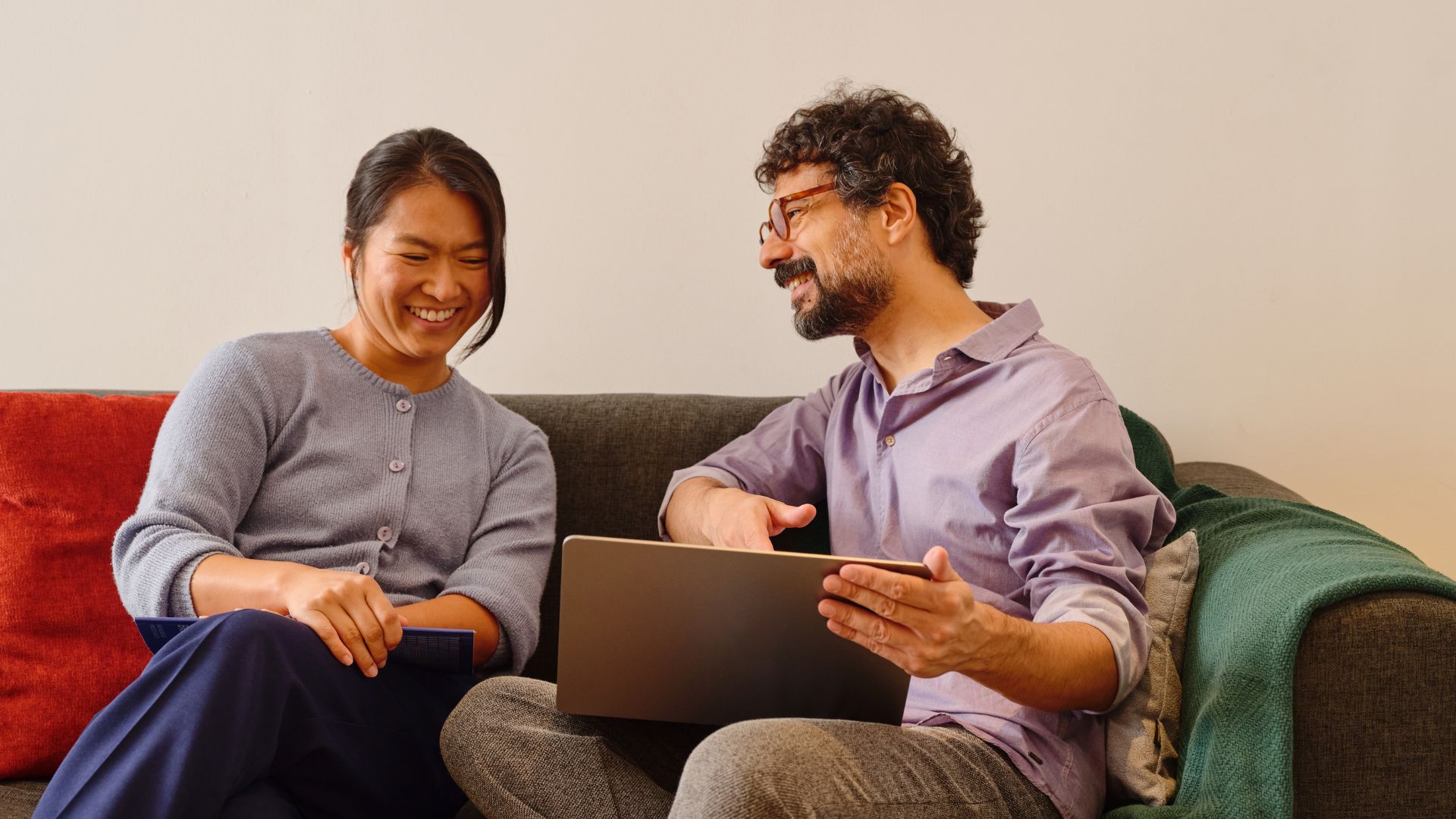 Två personer sitter i soffa och diskuterar med laptop